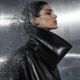 Illustration of a model in a black coat dissolving into particles against a steel backdrop.